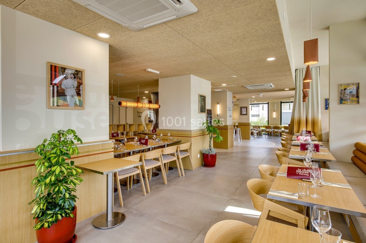 Salle de restaurant lumineuse avec tables en bois, chaises modernes, plantes décoratives et grandes fenêtres.