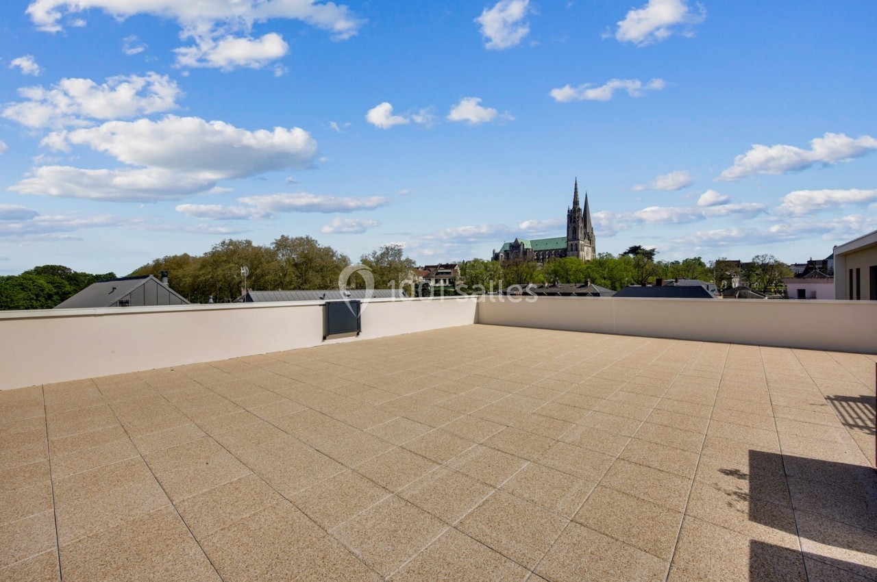 Terrasse spacieuse avec vue dégagée sur des toits et une cathédrale sous un ciel bleu parsemé de nuages.