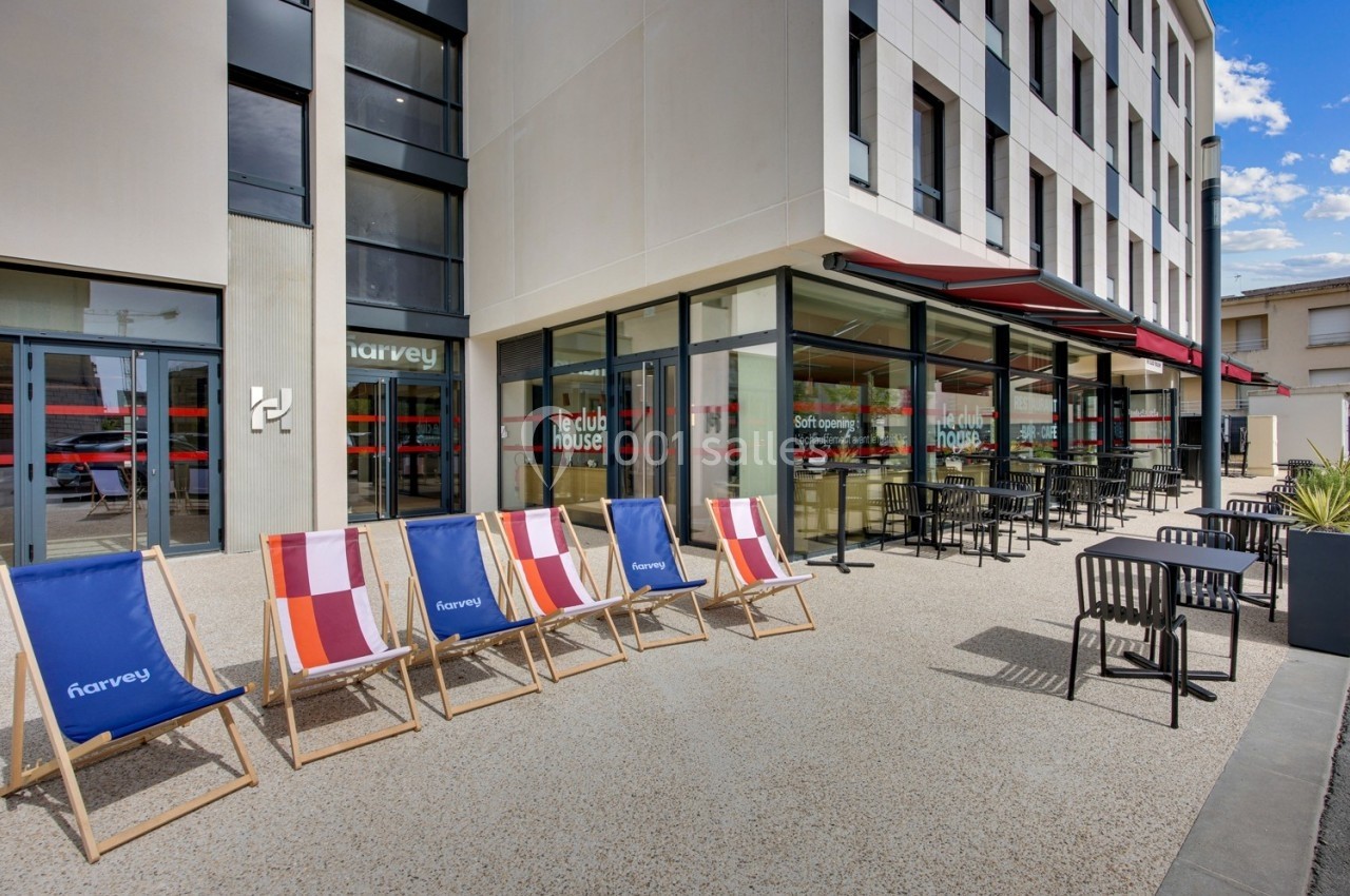 Façade moderne d'un bâtiment avec terrasse équipée de chaises longues colorées et tables en extérieur.