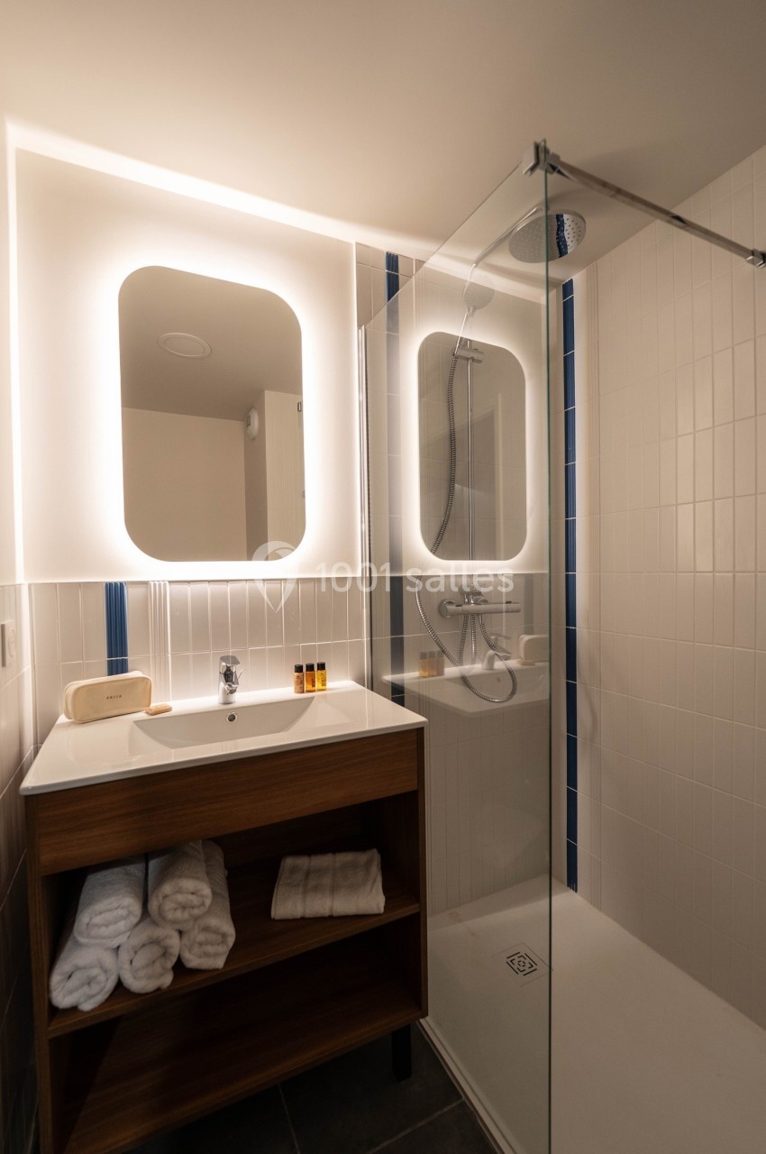 Salle de bain moderne avec douche à l'italienne, lavabo sur meuble en bois et miroirs éclairés.