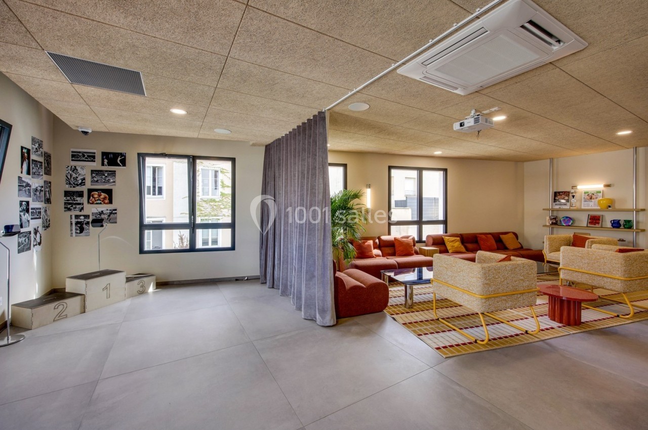 Espace lumineux avec coin salon coloré, fauteuils, canapé, plantes et photos accrochées au mur.