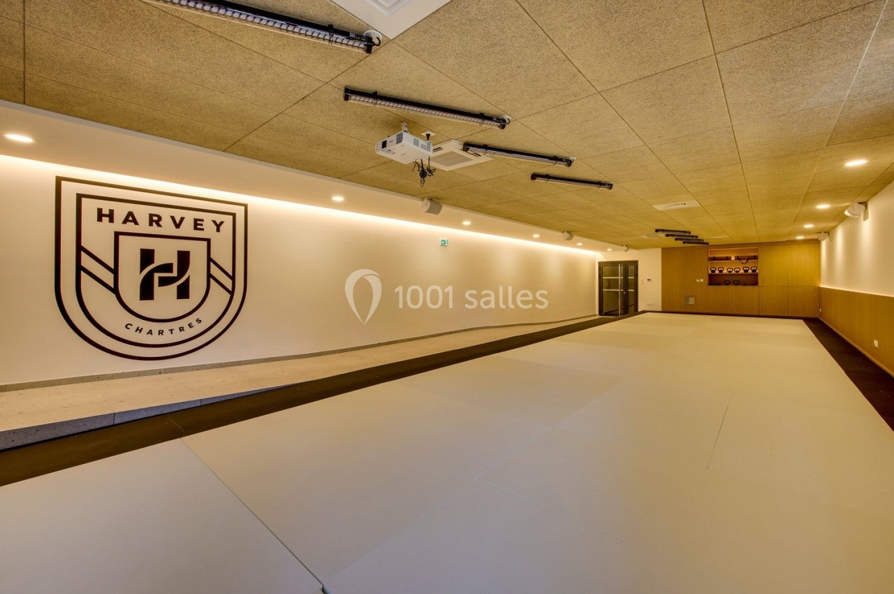 Salle intérieure spacieuse avec un sol clair, un logo mural ’Harvey Charter’ et un éclairage encastré.