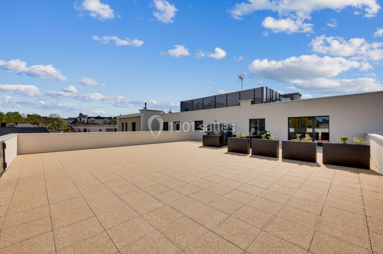 Terrasse spacieuse avec sol en dalles beige, jardinières modernes et vue dégagée sous un ciel partiellement nuageux.
