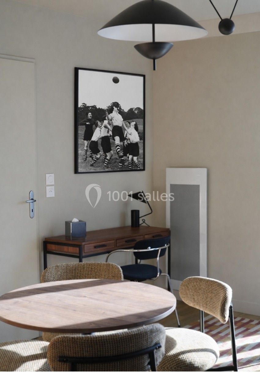 Salle à manger lumineuse avec table ronde en bois, chaises rembourrées, bureau en arrière-plan et photo encadrée au mur.