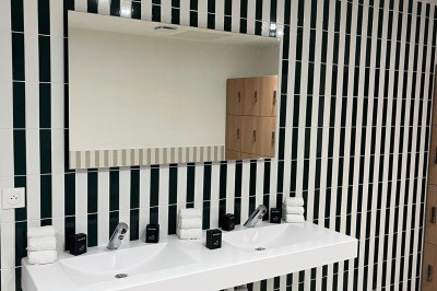 Salle de bain moderne avec douche à l'italienne, meuble en bois avec lavabo, miroir éclairé et serviettes pliées.