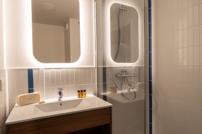 Salle de bain moderne avec douche à l'italienne, meuble en bois avec lavabo, miroir éclairé et serviettes pliées.