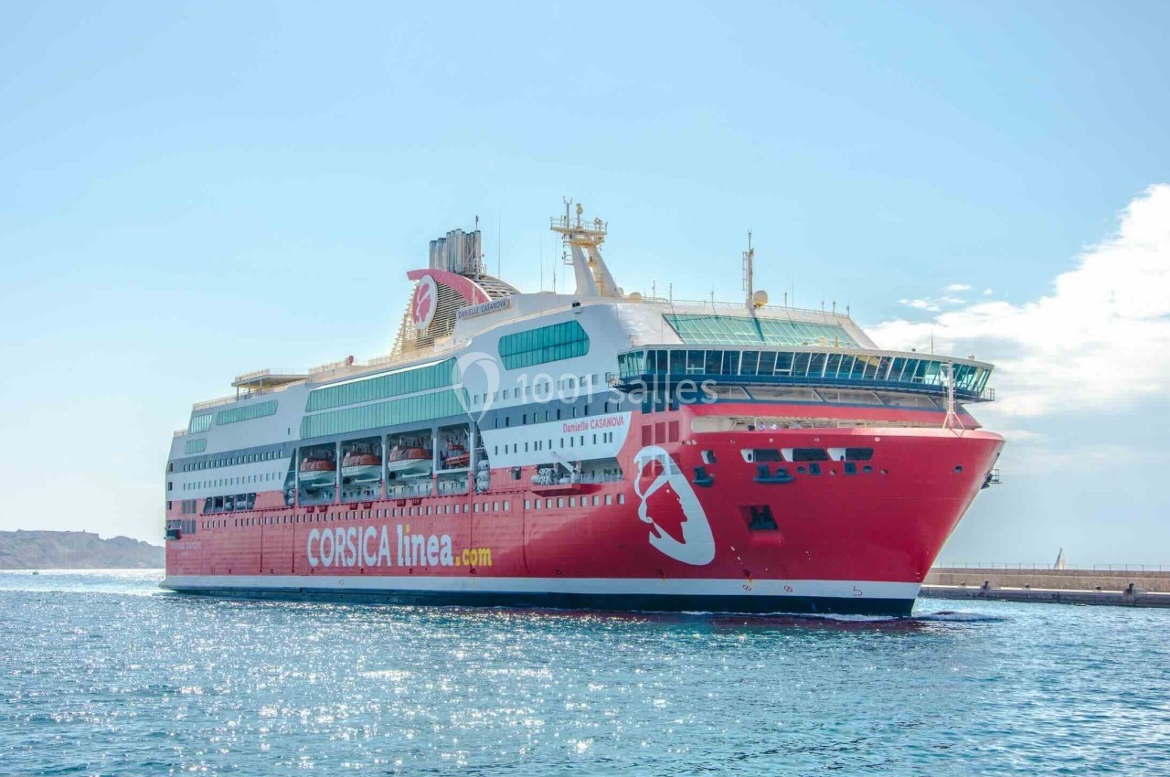 Ferry rouge de Corsica Linea naviguant sur une mer calme, avec un ciel dégagé en arrière-plan.