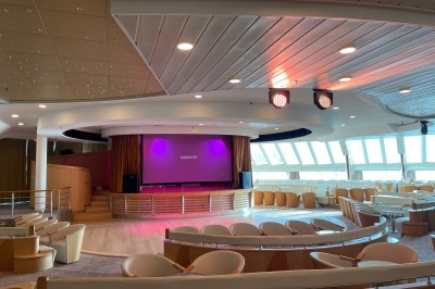 Salle de conférence vide avec rangées de sièges bleus et une estrade équipée de micros en arrière-plan.