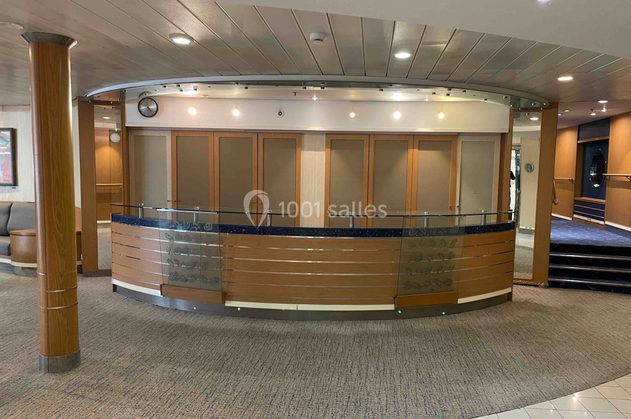 Comptoir d'accueil en bois et métal dans un espace intérieur avec éclairage intégré et sol en moquette.