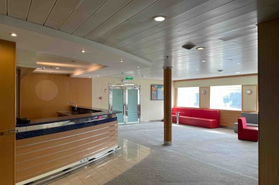 Salle de conférence vide avec rangées de sièges bleus et une estrade équipée de micros en arrière-plan.