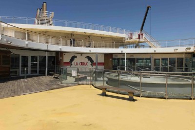 Salle de conférence vide avec rangées de sièges bleus et une estrade équipée de micros en arrière-plan.