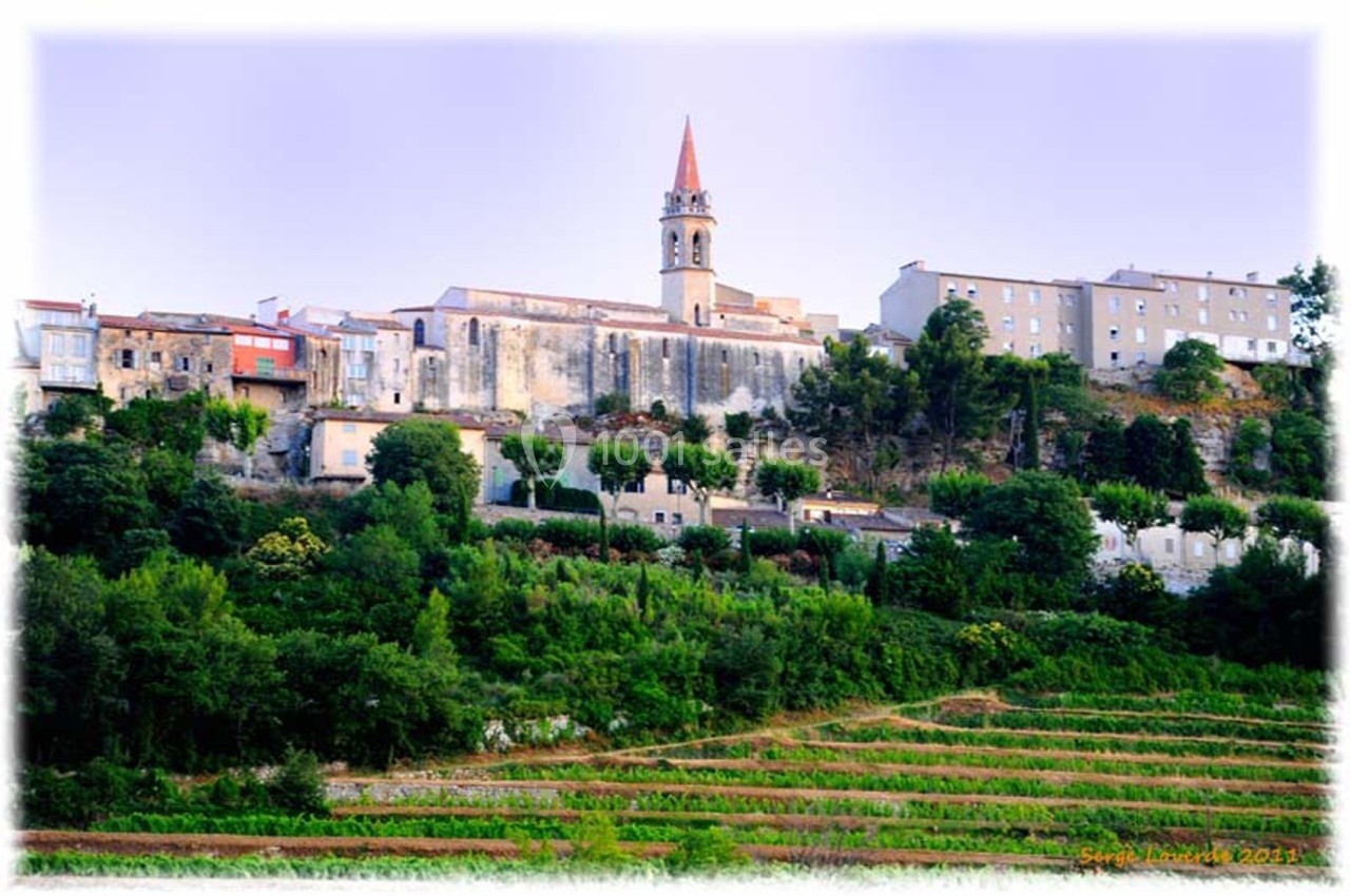 Village perché avec église au clocher rouge, entouré de maisons et de terrasses verdoyantes en premier plan.