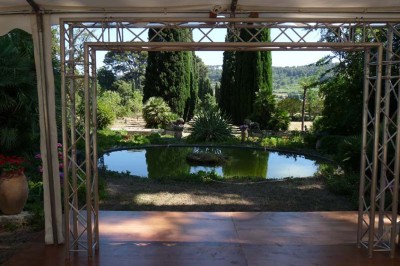 Miniature Location salle La Cadière-d'Azur (Var) - Château de Rochebelle - Var #8 Jardin verdoyant avec des pots en terre cuite et une tente blanche entourée d'arbres et de végétation.