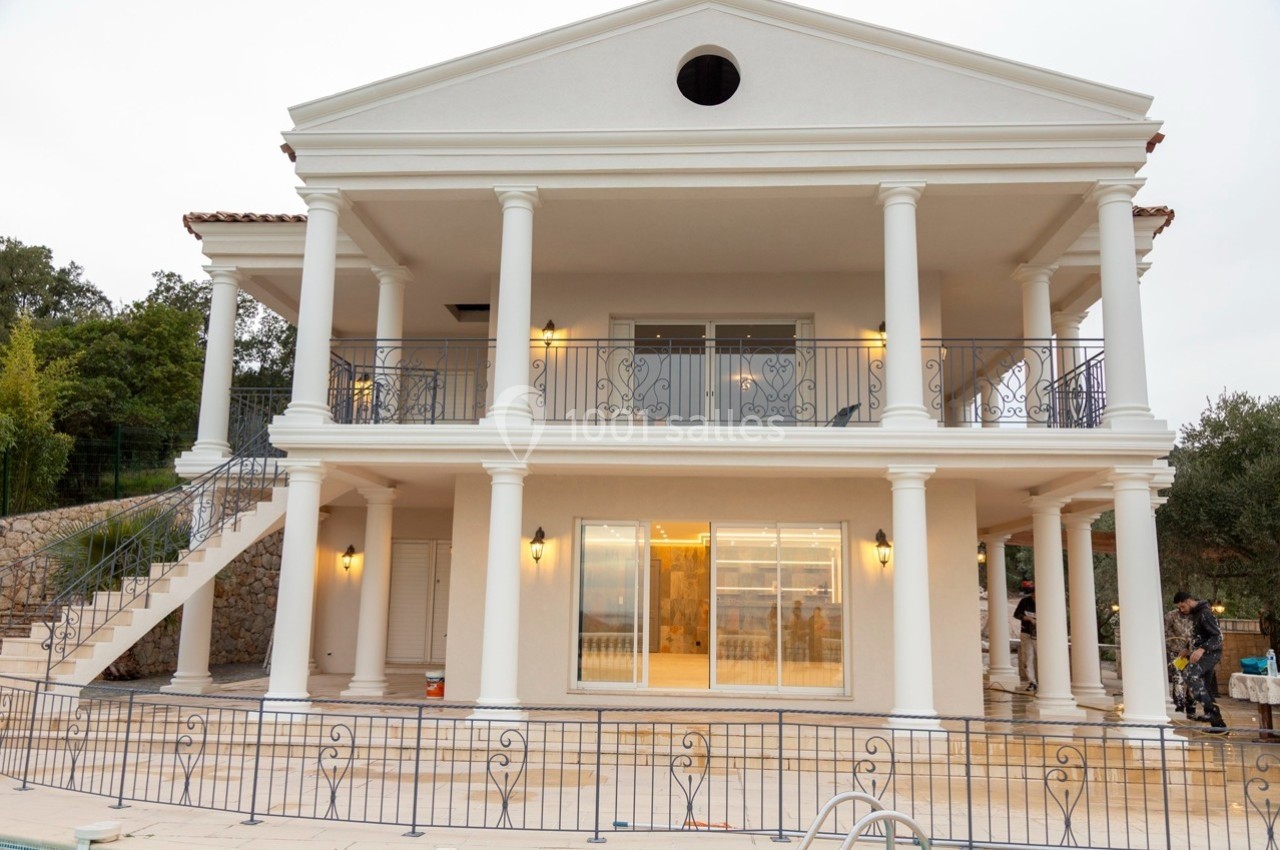 Façade d'une maison à deux étages de style classique avec colonnes blanches et balustrades en fer forgé.
