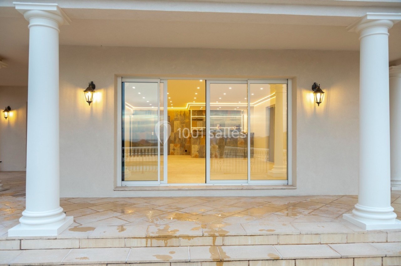Façade d'une maison avec une grande baie vitrée coulissante, encadrée par des colonnes et éclairée par des appliques murales.