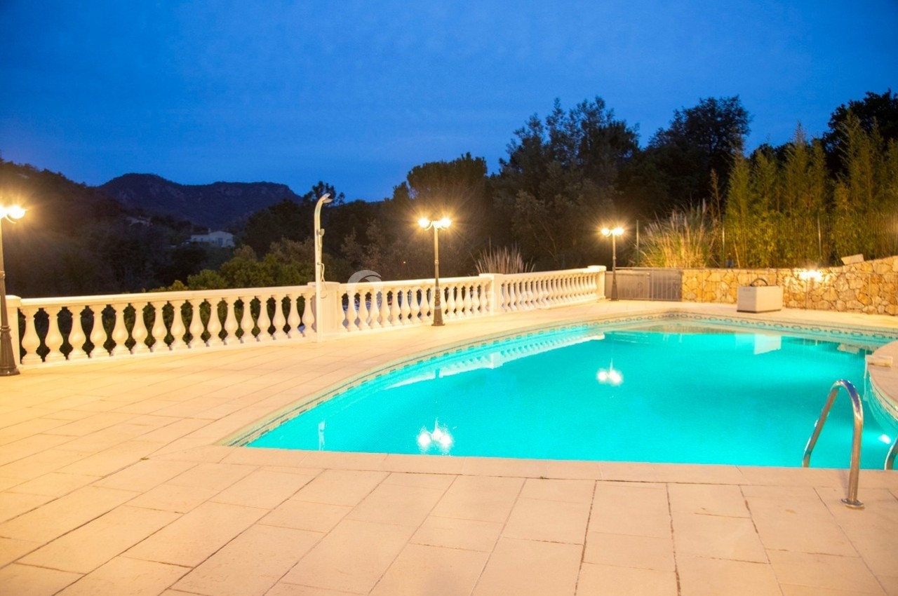 Piscine extérieure éclairée en soirée, entourée d'une terrasse en pierre et de balustrades blanches, avec vue sur des…