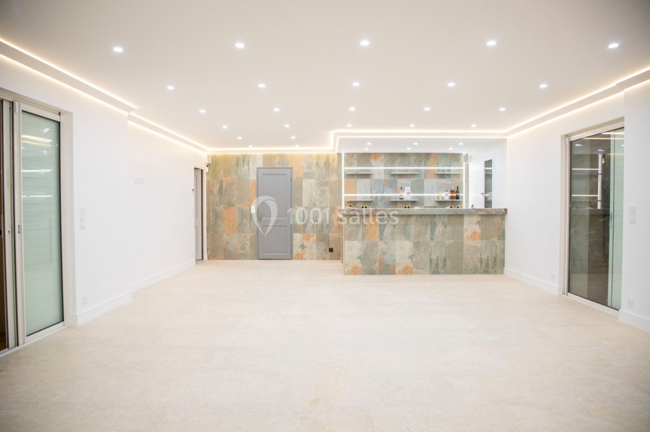 Salle lumineuse avec un sol clair, un mur en pierre naturelle, un bar intégré et des spots encastrés au plafond.