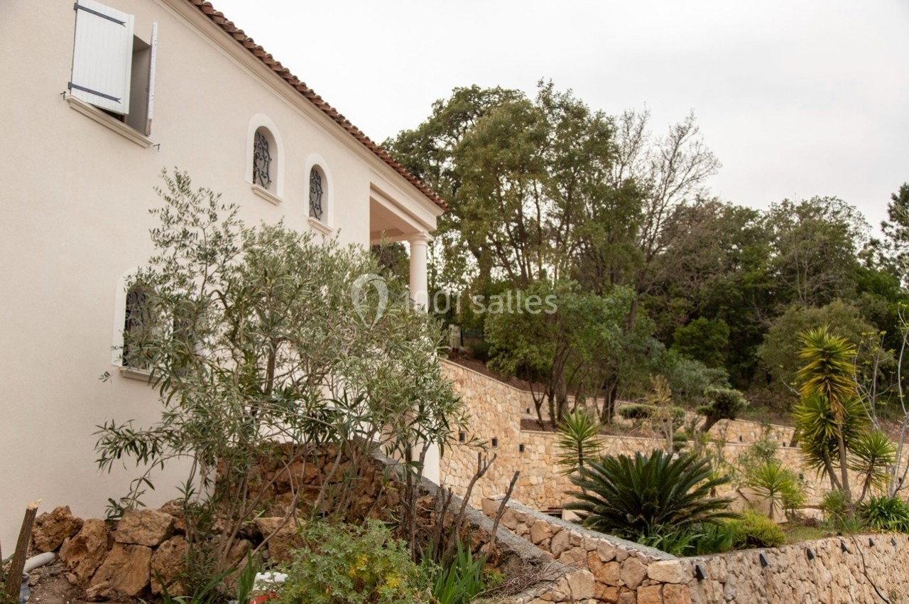 Façade d'une maison claire entourée d'un jardin méditerranéen avec des murs en pierre et des arbres.