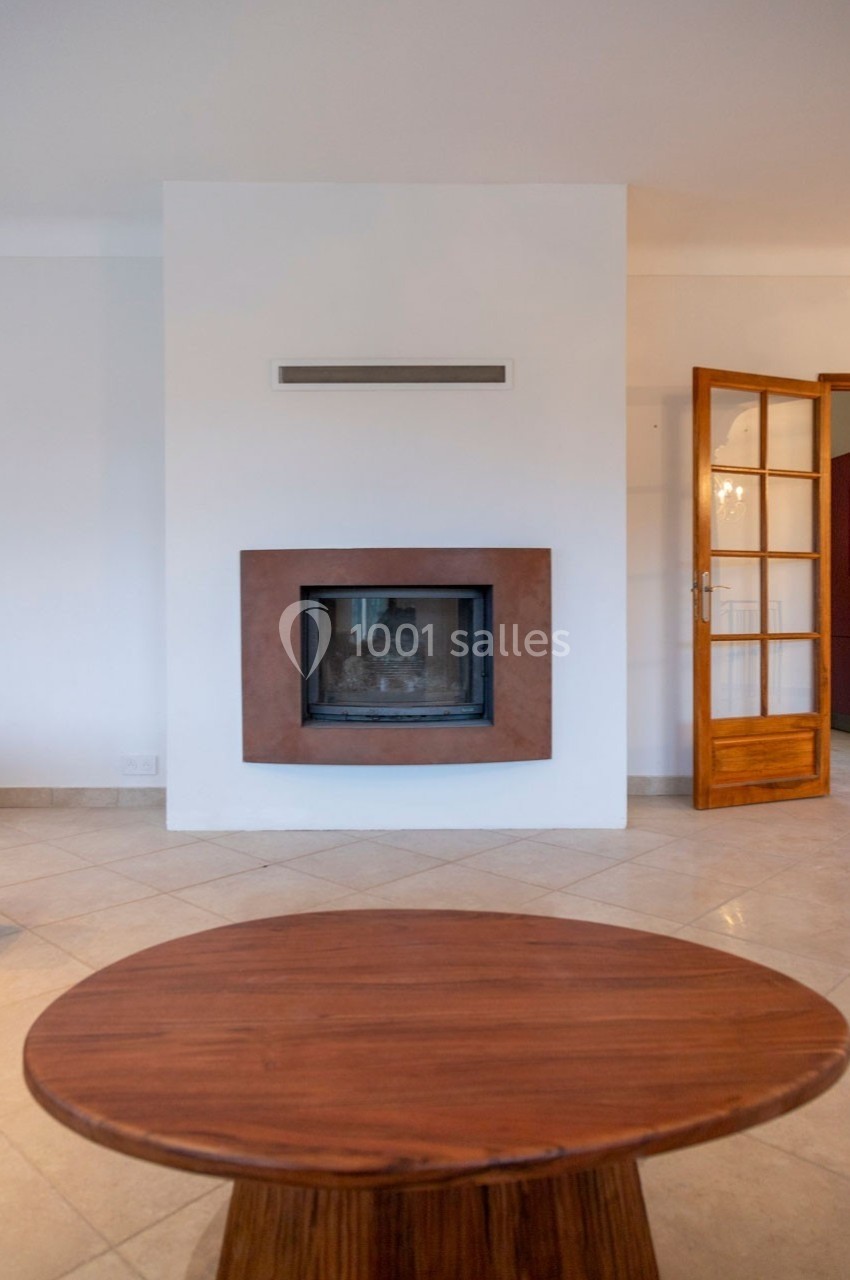 Cheminée moderne encastrée dans un mur blanc, avec une table basse en bois au premier plan et une porte vitrée à droite.