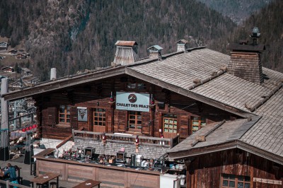 Une femme souriante se tient derrière une table en bois garnie de plats dans un chalet en bois éclairé chaleureusement.