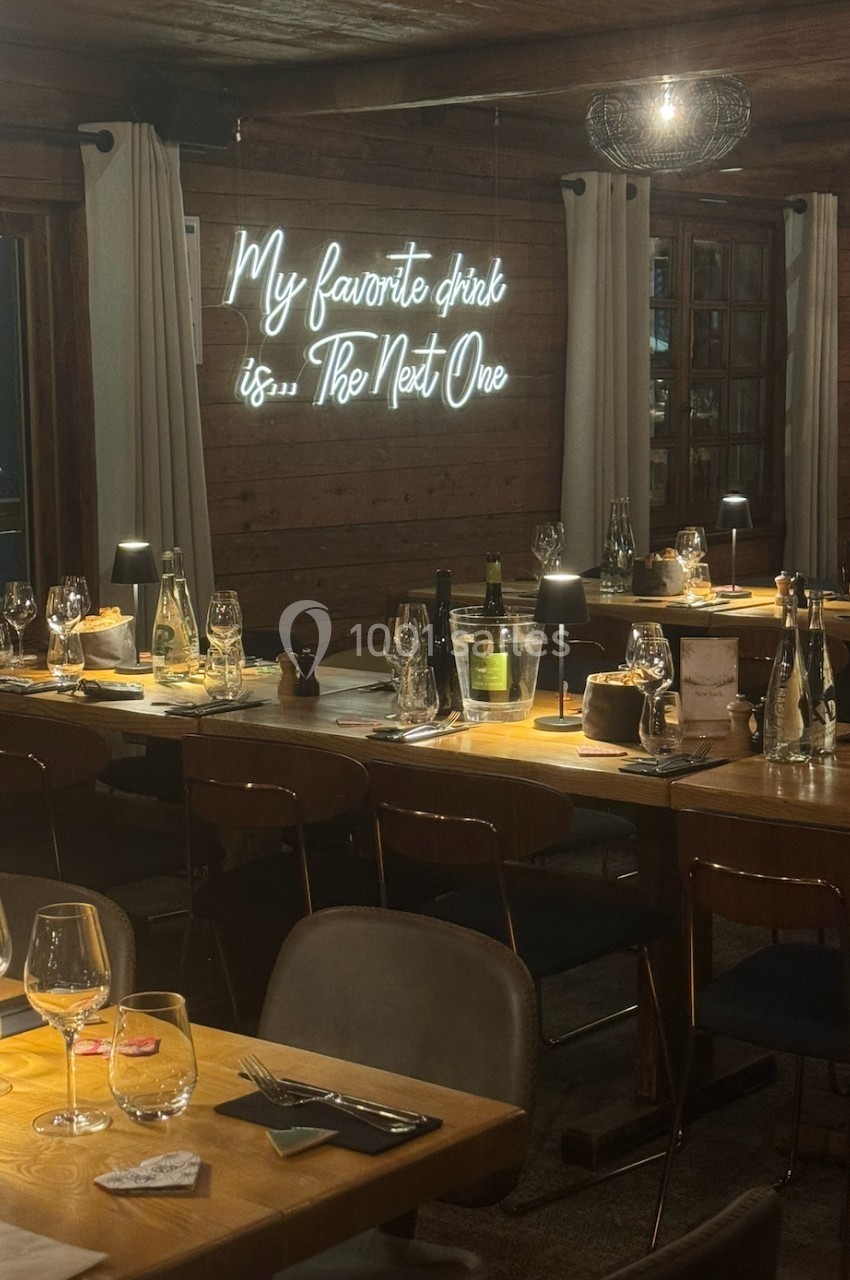 Salle de restaurant chaleureuse avec tables en bois, verres dressés et néon mural indiquant ’My favorite drink is... The…