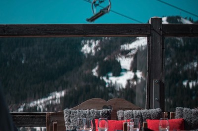 Une femme souriante se tient derrière une table en bois garnie de plats dans un chalet en bois éclairé chaleureusement.