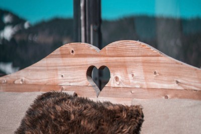 Une femme souriante se tient derrière une table en bois garnie de plats dans un chalet en bois éclairé chaleureusement.