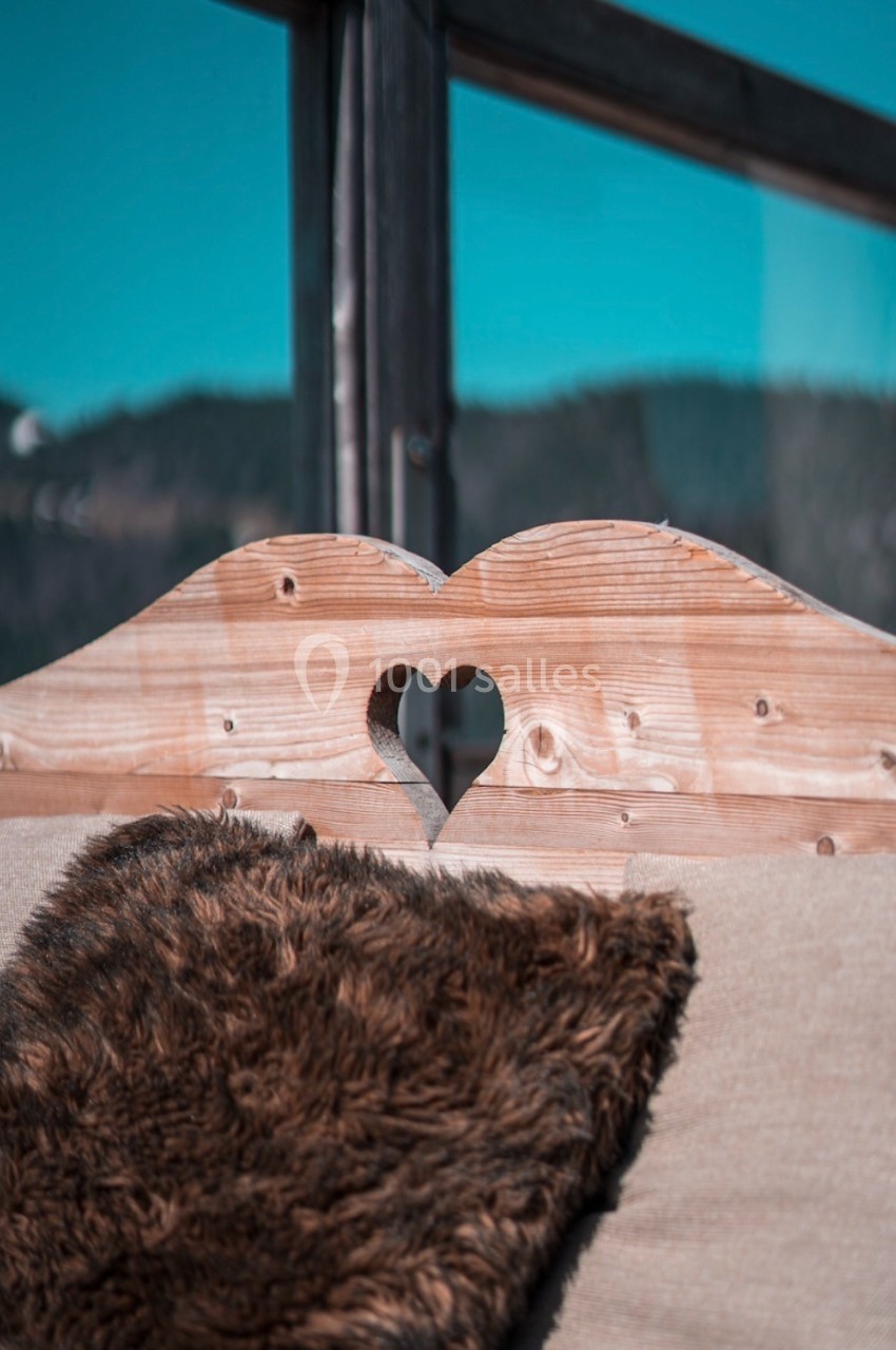 Dossier en bois sculpté d'un cœur, avec un coussin en fausse fourrure, devant une fenêtre donnant sur un paysage montagneux.