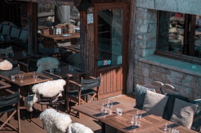 Une femme souriante se tient derrière une table en bois garnie de plats dans un chalet en bois éclairé chaleureusement.