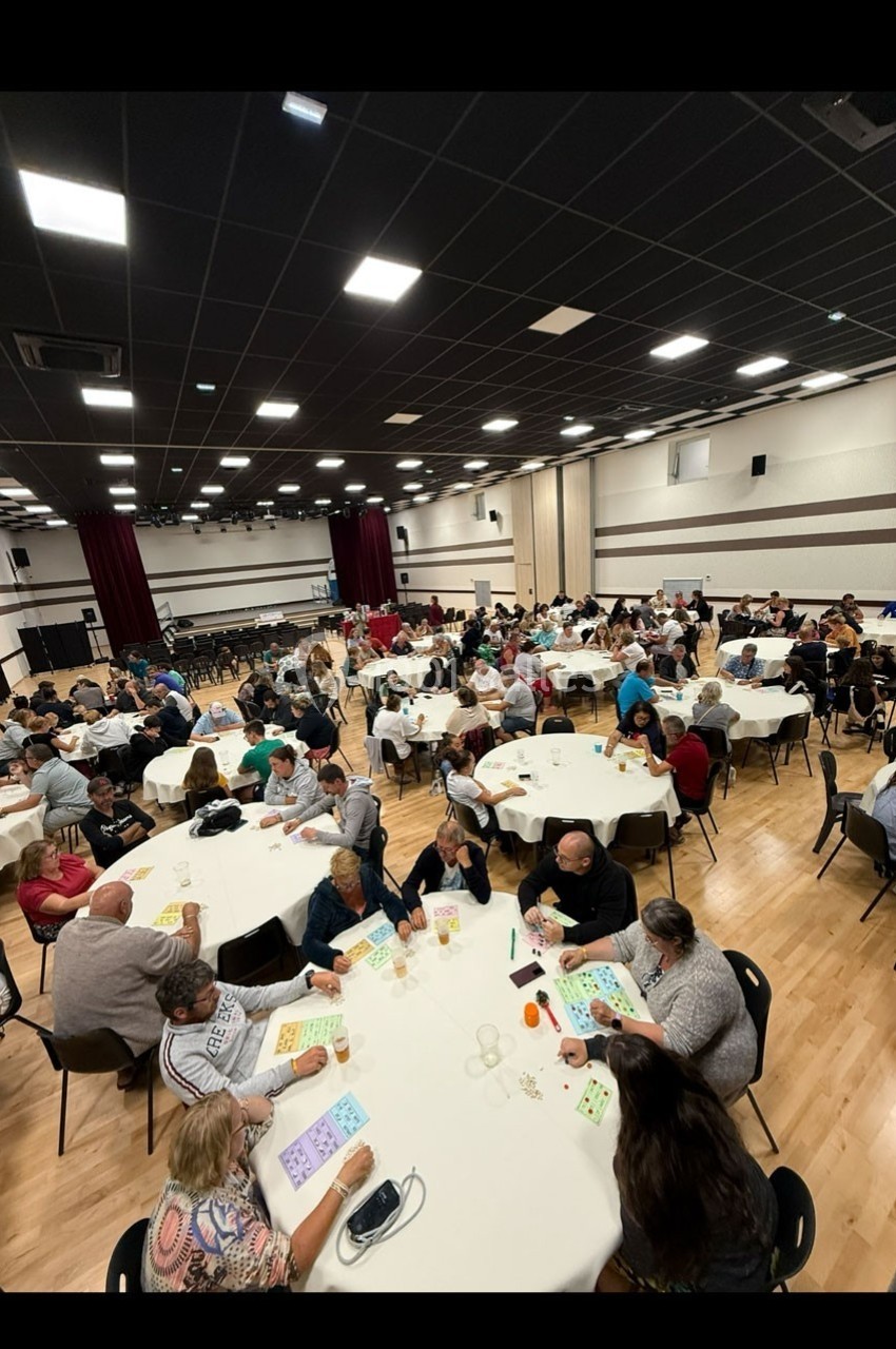 Salle remplie de personnes assises à des tables rondes, jouant au bingo dans une ambiance conviviale.