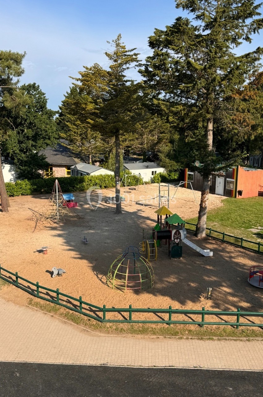 Aire de jeux extérieure avec structures pour enfants, entourée d'arbres et de clôtures en bois.