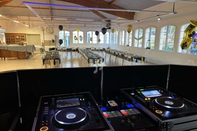 Salle de réception décorée avec des ballons noirs et dorés, vue depuis une table de mixage avec platines DJ.