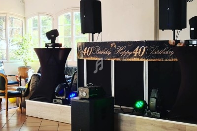 Table de mixage et enceintes installées dans une salle décorée pour un 40e anniversaire, avec éclairage et matériel audio.