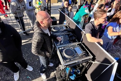 Un DJ mixe en plein air lors d'un événement festif, entouré de participants déguisés et de confettis.