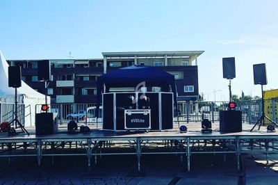 Scène extérieure avec équipement audio et éclairage, installée sur un quai pavé par temps ensoleillé.