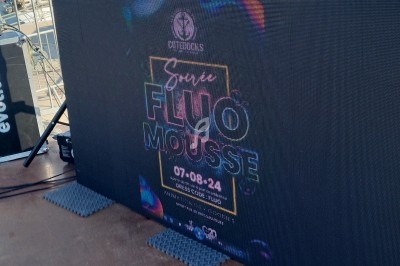 Panneau numérique annonçant une soirée fluo mousse prévue le 7 août 2024, installé en extérieur près d'un port.