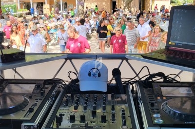 Vue depuis une table de mixage avec platines et ordinateur, face à une foule participant à un événement en plein air.