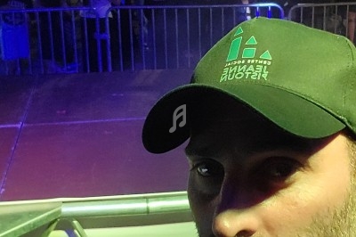 Un DJ mixe sur une scène en plein air la nuit, avec une foule en arrière-plan sous des éclairages colorés.