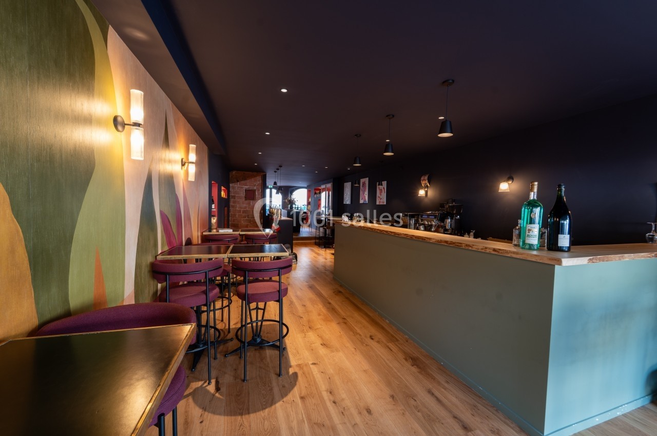 Intérieur d'un bar moderne avec un comptoir en bois, des tables hautes et une décoration murale colorée.