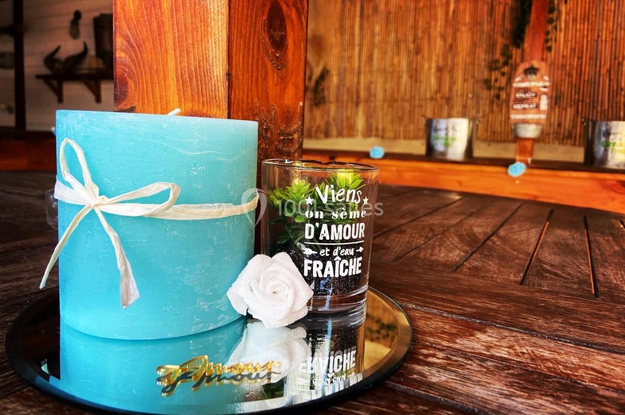 Bougie bleue et verre décoratif sur un plateau miroir, posés sur une table en bois dans un espace à la décoration naturelle.