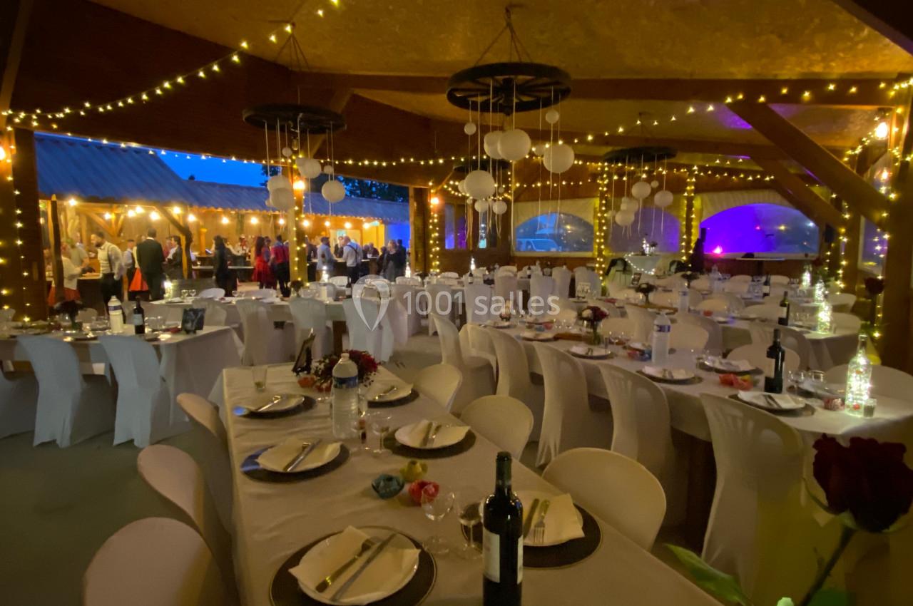 Salle de réception décorée avec des guirlandes lumineuses, tables dressées et invités en arrière-plan.