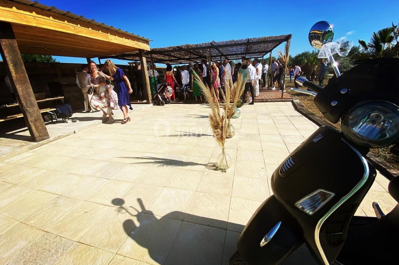 Un rassemblement en extérieur sous une pergola, avec des invités debout et un scooter au premier plan.