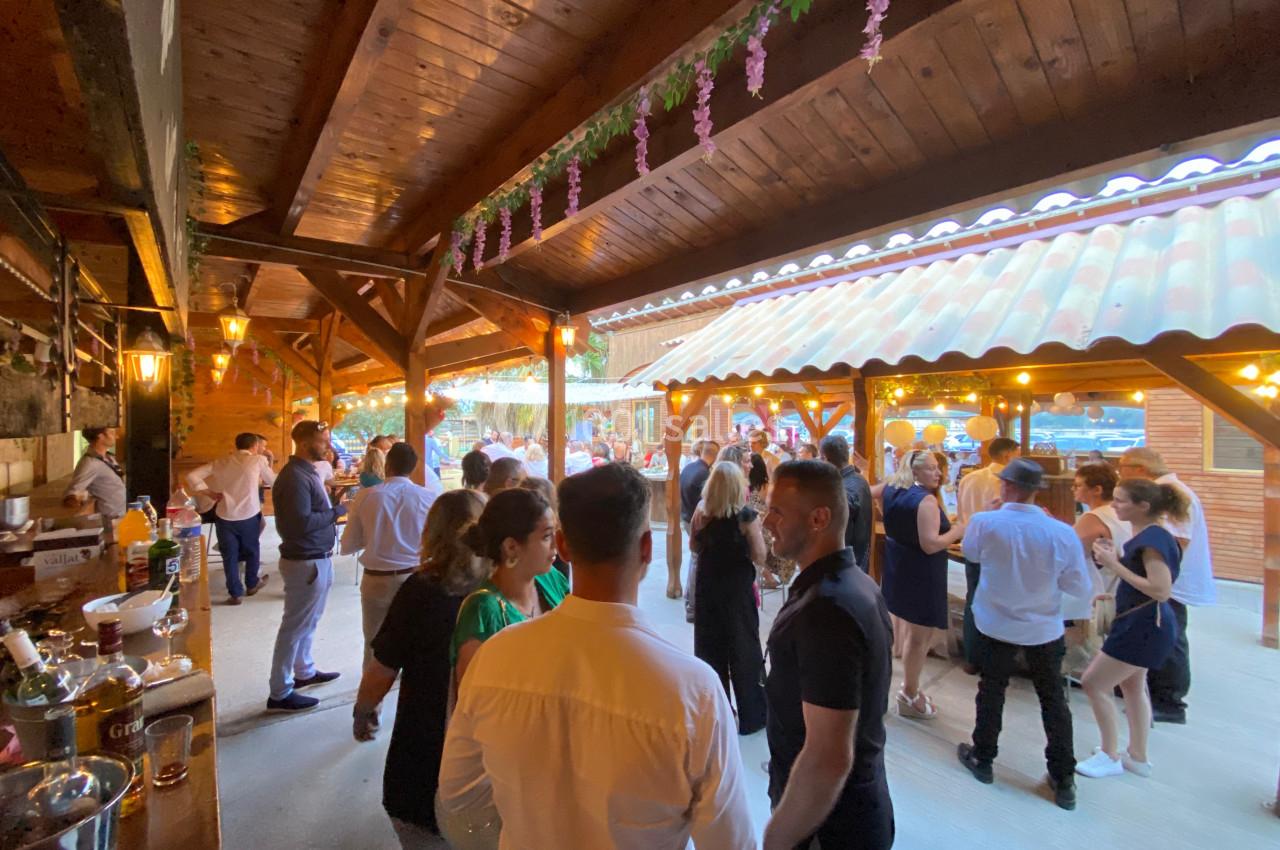 Personnes rassemblées dans un espace extérieur couvert en bois, discutant et dansant lors d'un événement festif.
