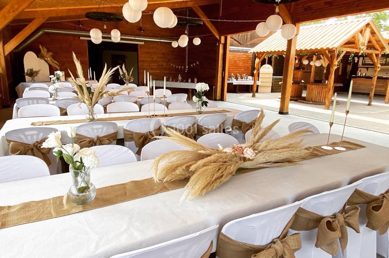 Salle de réception décorée avec des tables habillées de nappes blanches, ornées de centres de table en fleurs séchées et…