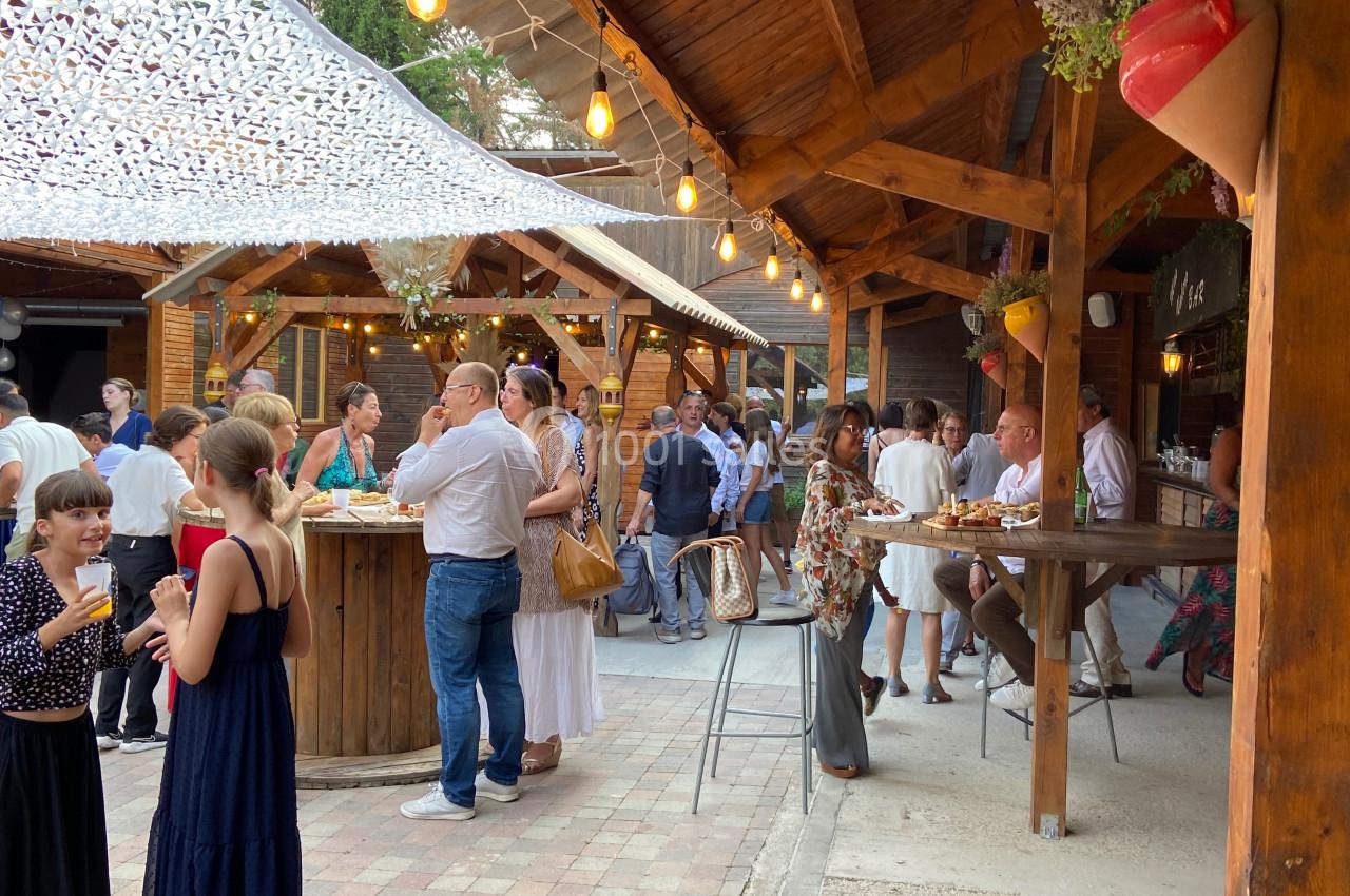 Groupe de personnes discutant et partageant un repas dans une ambiance conviviale sous une structure en bois éclairée.