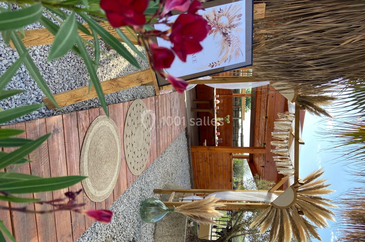 Chemin en bois bordé de plantes menant à une structure en bois décorée de fleurs séchées dans un jardin.