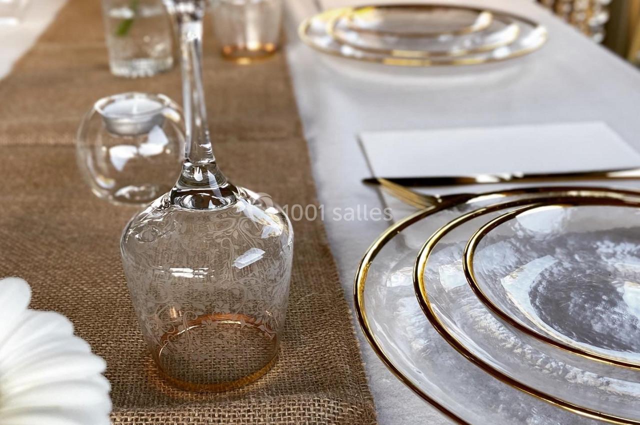 Table élégamment dressée avec des assiettes en verre, des verres à pied et une nappe en toile de jute.
