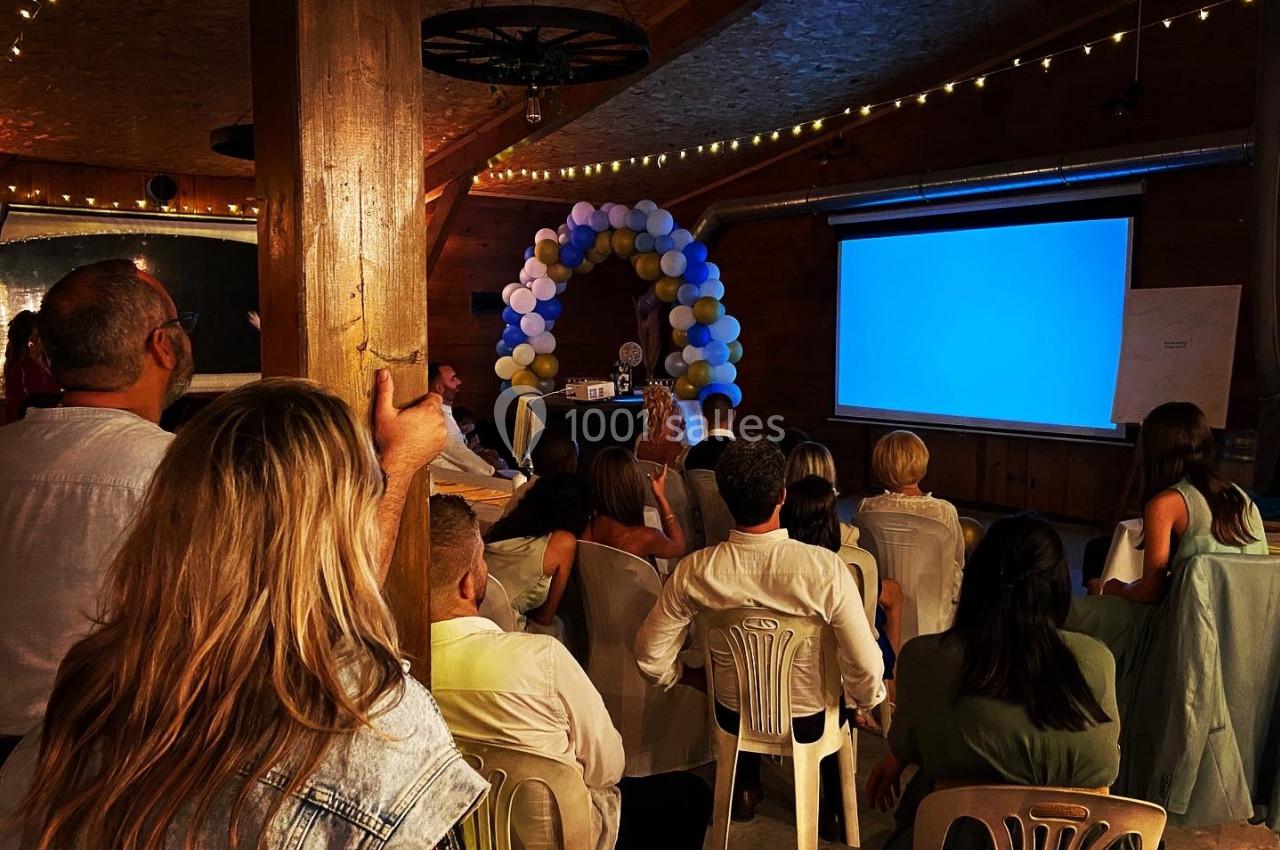 Un groupe de personnes assises dans une salle décorée, regardant une présentation projetée sur un écran.
