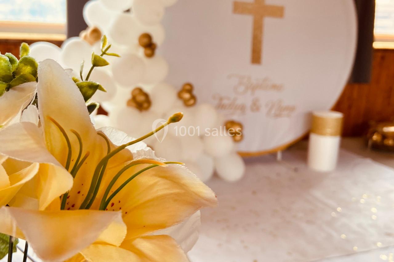 Arrangement floral au premier plan avec en arrière-plan une décoration de baptême composée de ballons blancs et dorés.