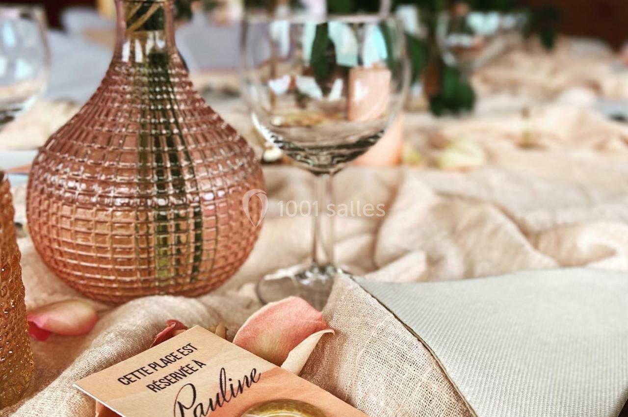 Table décorée avec des fleurs, verrerie et un marque-place personnalisé avec un sceau doré et le prénom ’Pauline’.